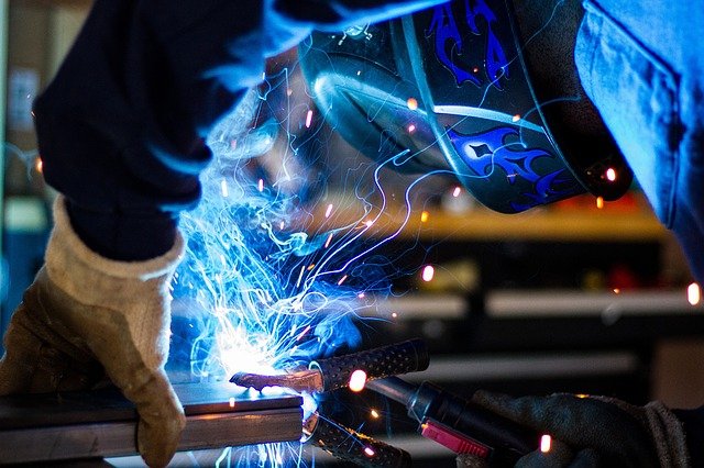 Machine operator working on a welding project while smoke and sparks emit.