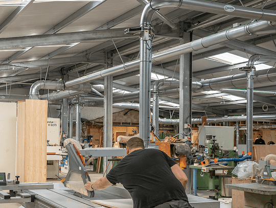 Woodworker working on a project in a large commercial facility with ductwork installed for dust collection.